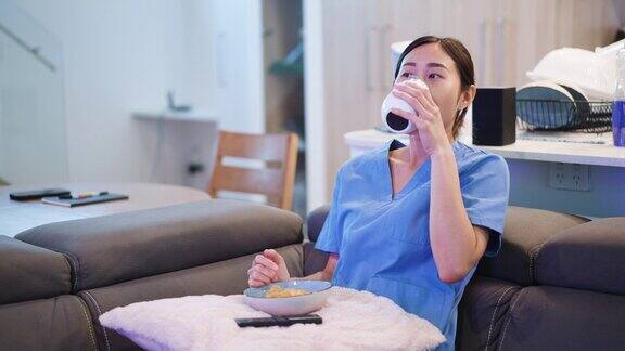 年轻的成年亚洲女性保健工作者穿着磨砂服在公寓客厅休息和看电视