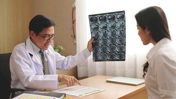 亚洲医生在医院拿着脑部x光片向病人解释偏头痛和脑癌的结果