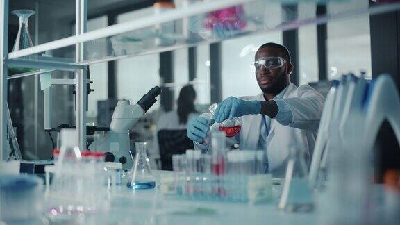 戴着护目镜的非裔美国男科学家在实验室的试管中混合化学物质英俊的黑色微生物学家工作在现代实验室与技术设备