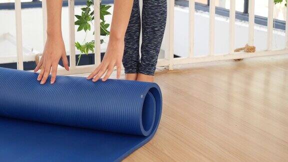 女子双手卷起瑜伽垫在瑜伽健身训练室的健身房地板上家庭锻炼妇女近手滚动泡沫瑜伽体操垫妇女赤脚家庭锻炼体育健康的生活方式
