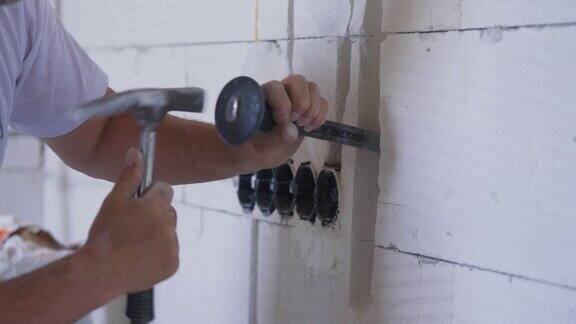 建筑工人用墙凿扩大电缆追逐槽手握工具和锤击细节