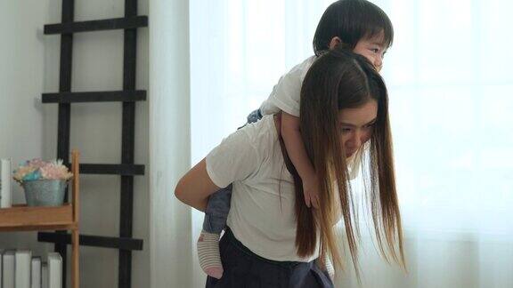 亚洲男婴拥抱并依偎在他年轻的母亲的背上
