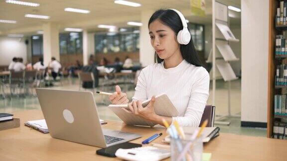年轻漂亮的亚洲学生在学校图书馆学习并使用笔记本电脑进行在线学习e-Learning教育理念回到学校