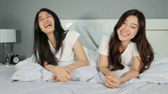 两个年轻的女朋友微笑着躺在床上聊天