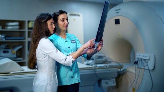 医务人员讨论x光照片两名女专家在医疗制服检查x光照片的背景在诊所的新设备