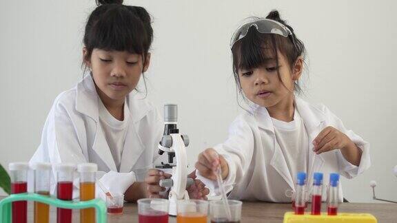 穿着实验室工作服的亚洲儿童在家庭学校实验室里使用显微镜进行科学实验