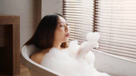 美丽的亚洲女人吹泡沫而在家里洗热水澡
