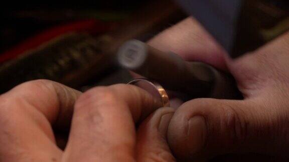 在手工制作金戒指的过程中珠宝商使用安装在柔性轴钻机上的砂纸卷来打磨金属