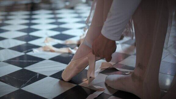美丽的年轻芭蕾舞女演员在工作室的地板上系着鞋子鞋子上有丝带