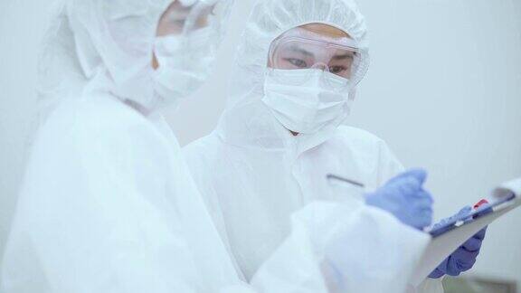 冠状病毒大流行期间两名身穿防护服的医务人员在剪贴板上讨论血液检测结果