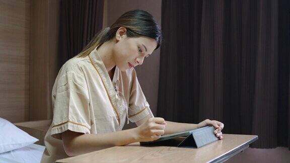 年轻的亚洲妇女在医院病床上用数字平板电脑工作