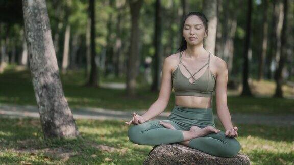 周末早上一名亚裔华裔妇女在公园里冥想练习瑜伽