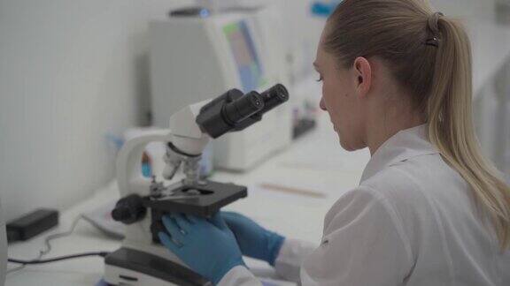 在实验室工作时使用显微镜的女科学家现代医学研究实验室女实验室助理看着显微镜分析样本生化物质验血