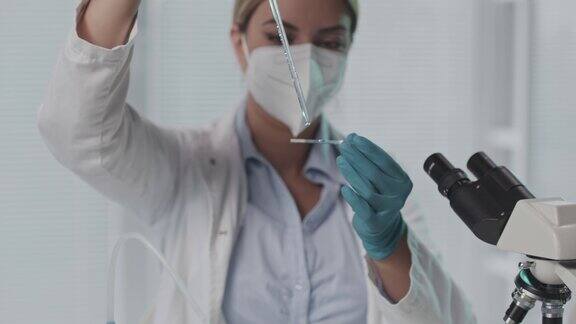 女实验室技术人员将一滴液体放在显微镜载玻片上准备进行分析