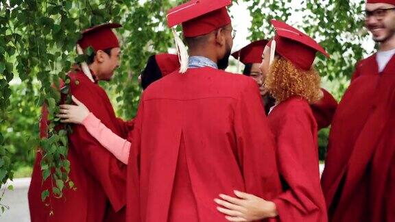 毕业典礼后快乐的朋友们穿着学士服和学位帽互相祝贺他们拥抱和大笑