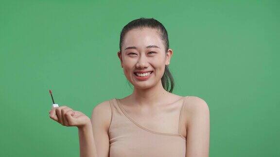 亚洲妇女涂口红然后微笑站在绿色屏幕背景在工作室