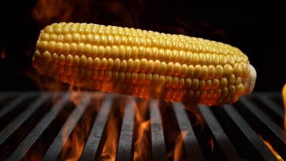 玉米棒子落在烤架格栅上燃烧在慢动作-烧烤在黑色背景