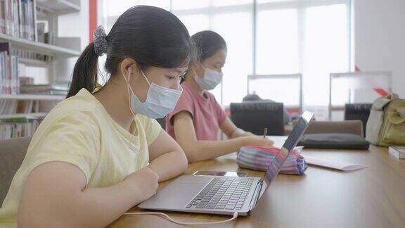 新常态亚洲女孩在图书馆网上学习戴口罩防止冠状病毒covid-19技术教育