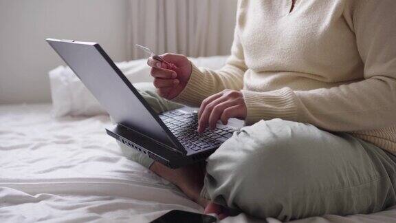 坐在床上的女人用信用卡和笔记本电脑在网上付款