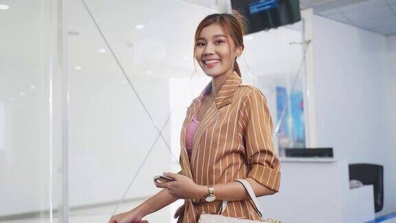 年轻美丽的女子乘客拿着护照和手提箱走在机场航站楼的登机口这个女孩微笑着看着相机对坐飞机出国旅行感到兴奋