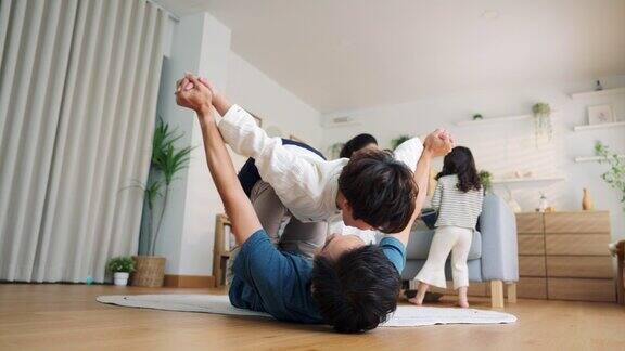 亚洲爸爸躺在客厅地板上和小儿子玩飞机