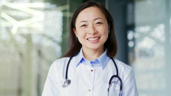 微笑的亚洲女儿科医生穿着白大褂戴着听诊器在现代医院的诊所里看着相机
