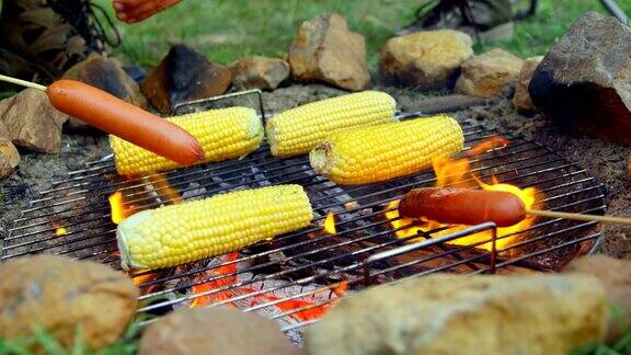 朋友们在篝火上烤热狗和玉米的特写
