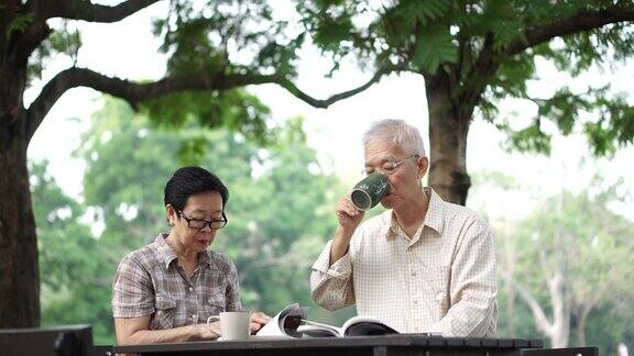 亚洲退休老年夫妇在公园喝咖啡和看书