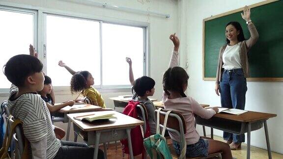 一群小学生拿着笔记本坐在教室里举手回答老师的问题教育小学学习回到学校