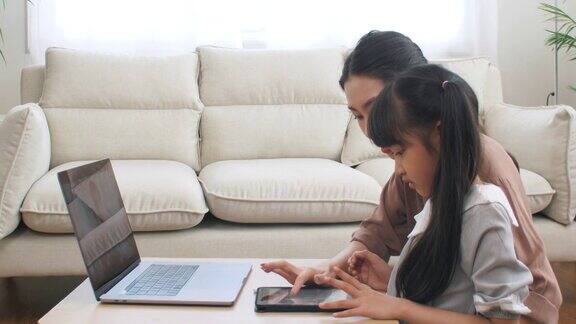 亚洲家庭与女儿学习在笔记本电脑和妈妈在客厅