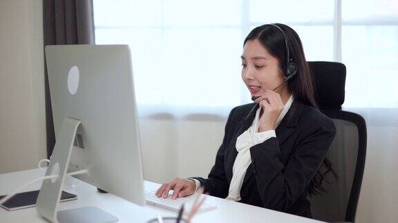 Smiley亚洲商务女接待员戴耳机视频会议电话在电脑上通过网络摄像头在网上聊天客户支持服务