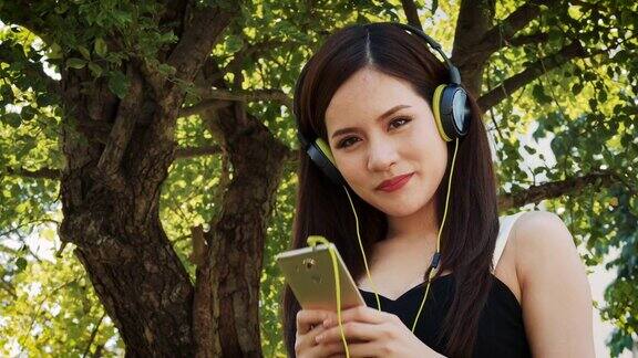 快乐的年轻人戴着耳机用智能手机听音乐站在户外的公园里
