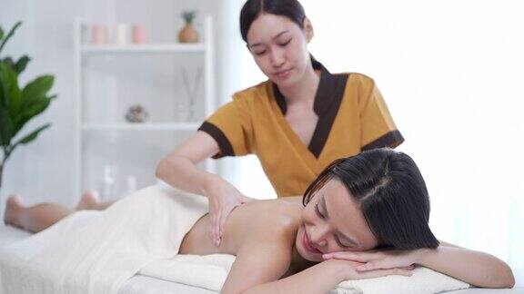 一个美丽的亚洲女人的肖像躺在按摩床上一个按摩师正专注地按摩女人的背部充满信心