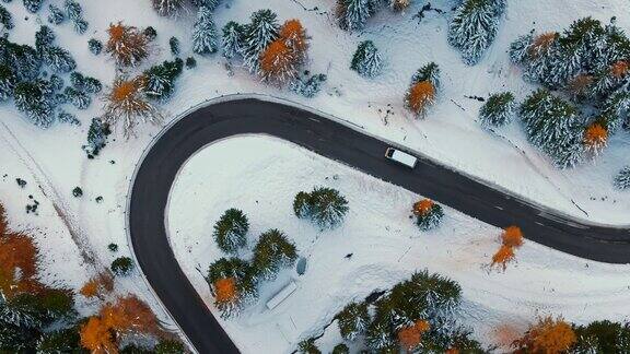 空中无人机拍摄的汽车行驶在蜿蜒的道路上穿过白雪覆盖的森林和山区景观在白云石