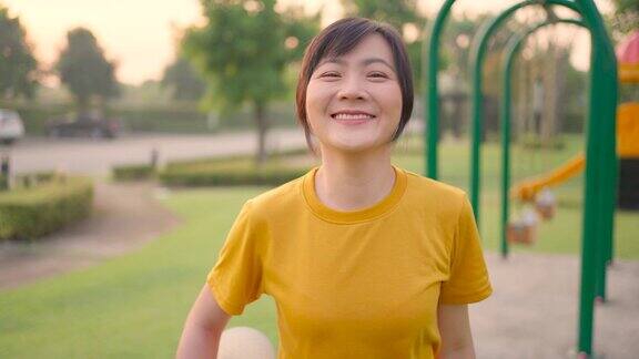 在公园里一名亚洲妇女穿着运动服抱着卷好的瑜伽垫开心地微笑着看着镜头