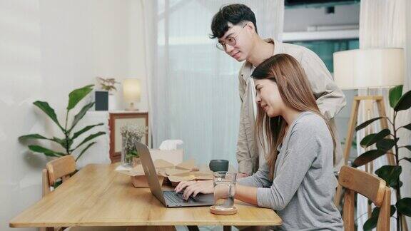 年轻的亚洲女性在家工作而她的男友好奇地看着她