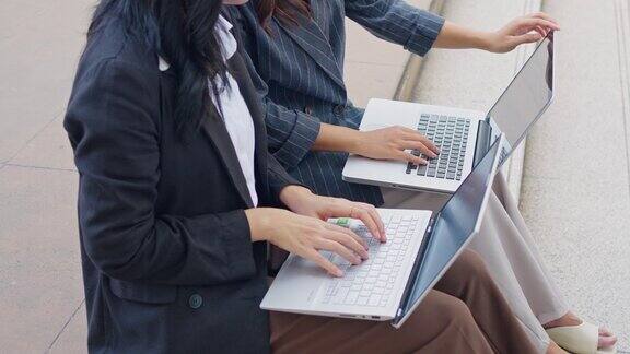 在办公室外使用笔记本电脑工作的商务人士两个年轻的亚洲女商务人士正在开会和同事一起讨论