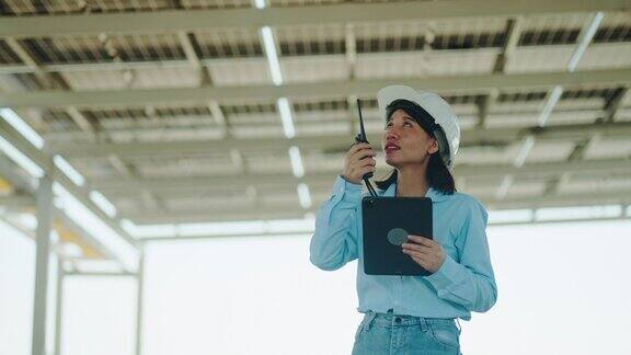 女工程师电工在检查屋顶上的太阳能电池板时使用手持对讲机