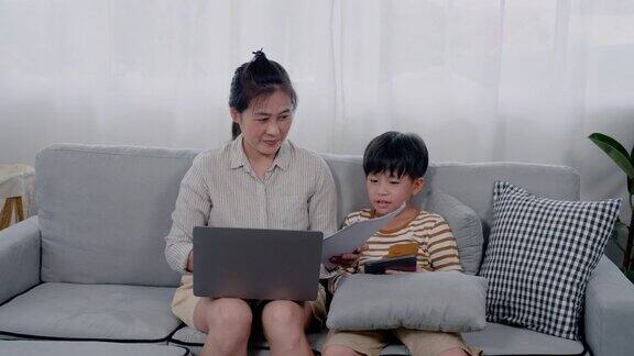 4K英俊的亚洲男孩和他的母亲正在笔记本电脑上工作小男孩生气了紧张地从他母亲的手中抽出纸想让她自己玩