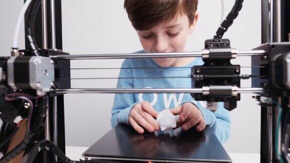 打印3D打印机雕像玩具从白色塑料特写男孩高兴而又激动地从打印机的工作平台上拿起打印好的图形进入了戏剧