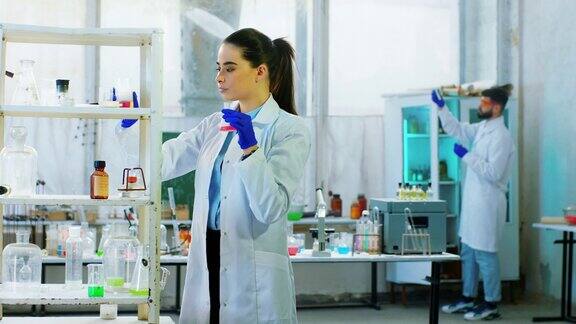 化学实验室迷人的女科学家工作在一个实验与她的助理男人使用一些化学液体在玻璃浴缸4k