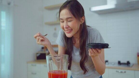 年轻的亚洲女人在家里的厨房里制作冰沙饮料