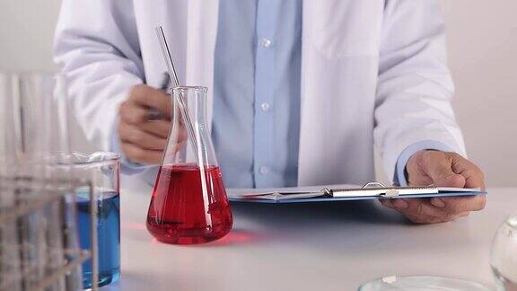 年轻科学家在实验室写实验结果和搅拌红色溶液