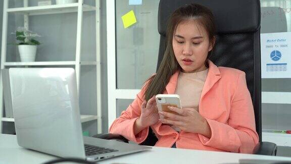 年轻的亚洲女商人在办公桌上使用笔记本电脑和手机