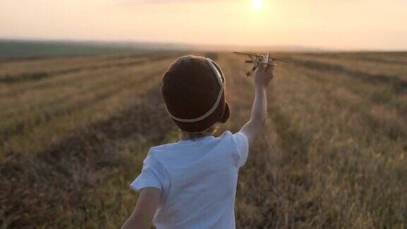 快乐的小男孩在头盔里的孩子飞机飞行员和玩具木制飞机在田野里奔跑