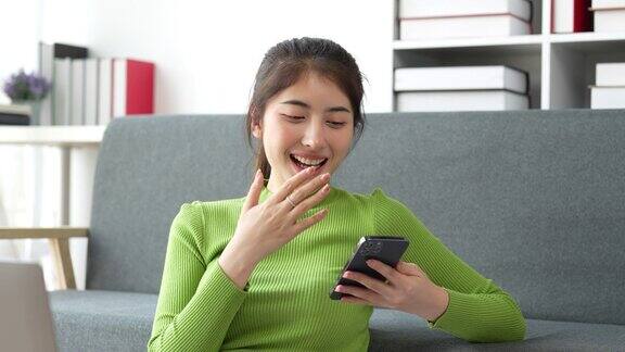 漂亮的亚洲女人坐在家里的沙发上享受与朋友的视频会议女人在家用智能手机制作内容高品质4k画面