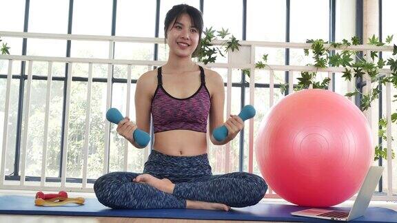 美丽的亚洲女性用哑铃锻炼肌肉的家庭健身女子举重训练用微笑练习普拉提球哑铃美女微笑着穿着运动服在瑜伽垫上健身