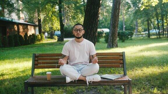 亚洲男子坐在长椅上冥想在早晨公园