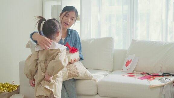 年轻的亚洲家庭的女儿祝贺妈妈并给她的明信片和礼物在客厅的乐趣在节日庆祝母亲节在家家庭幸福时刻