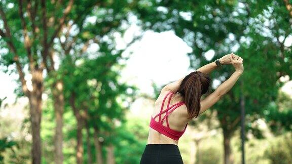 穿着粉红色运动服的年轻成年女性在公园户外伸展肌肉运动女性为早上跑步和慢跑做准备健康、健身、锻炼和工作与生活平衡
